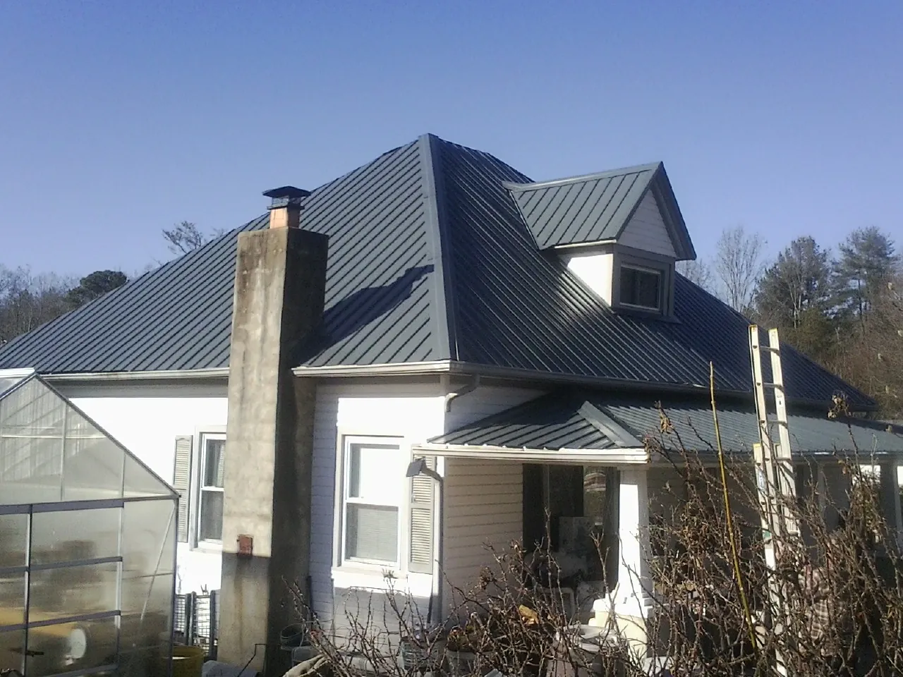 Dark blue standing seam metal roof on a white farmhouse with dormer — Slate & Tile Roof Repair by Roofing Brothers in Parsonsfield