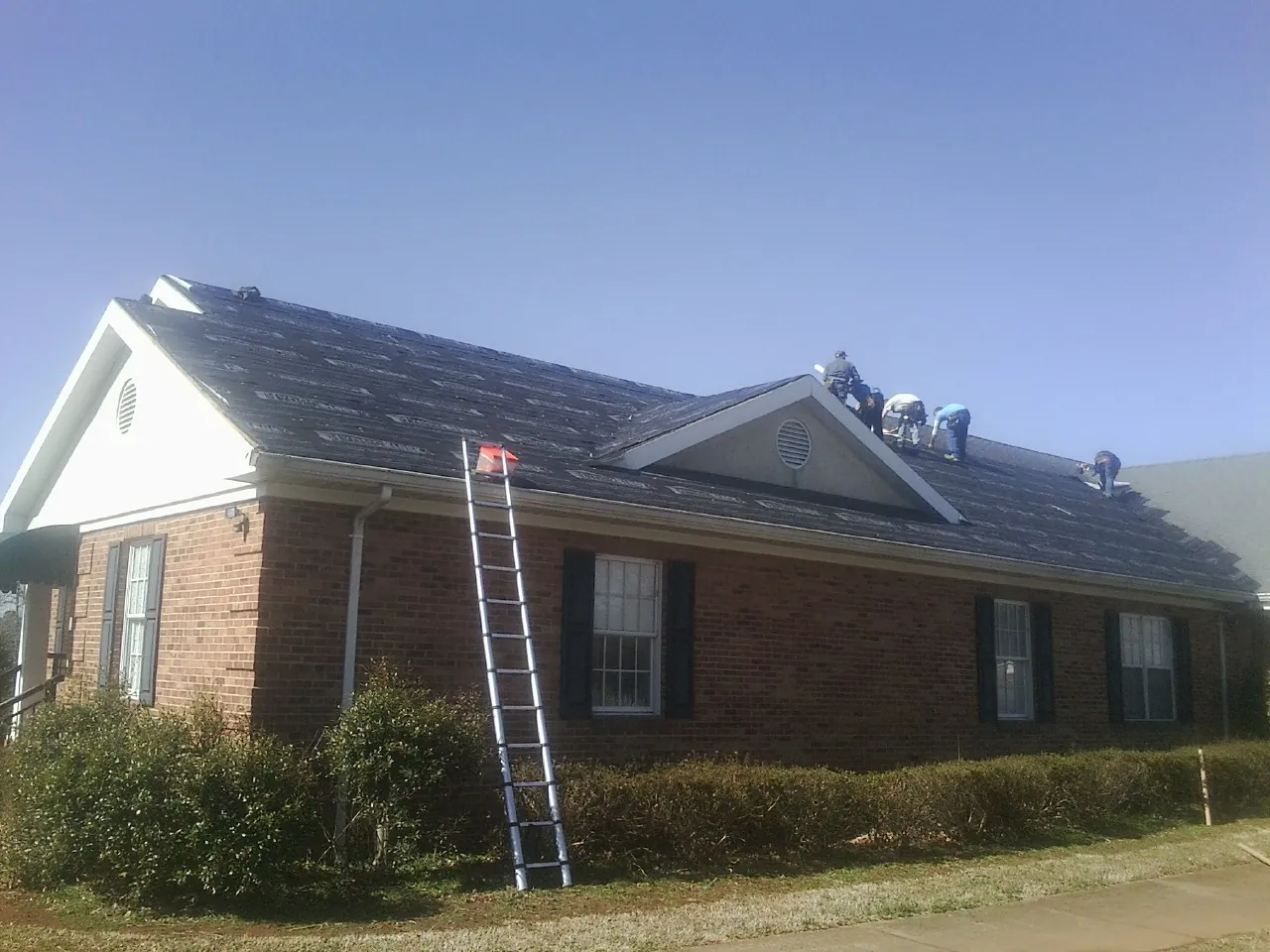Crew tearing shingles off a brick ranch roof with a ladder set — Metal Roof Repair work by our crew in Parsonsfield