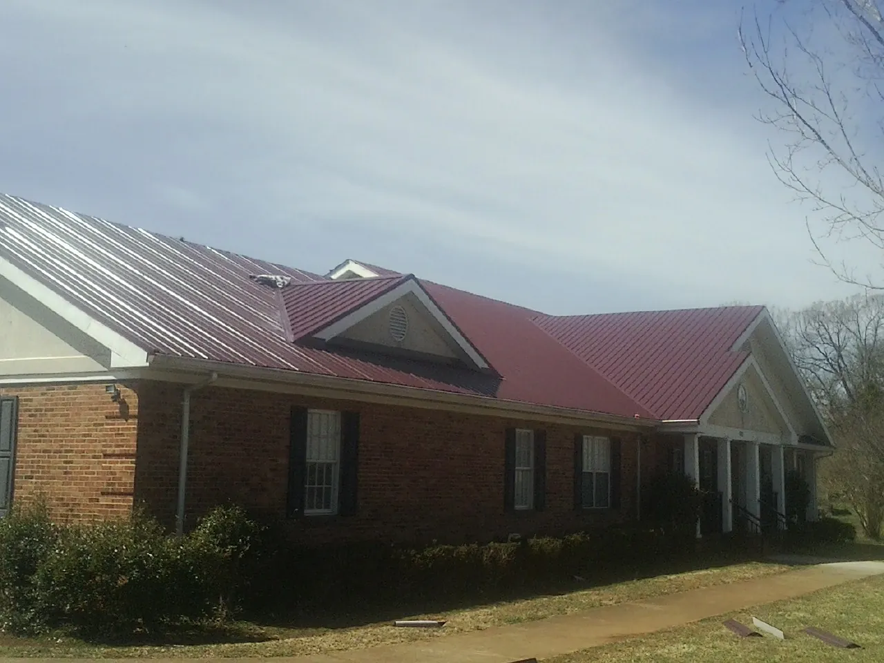 Red metal roof with gabled entries on a long brick building, from a Hail Damage Roof Repair job in Parsonsfield