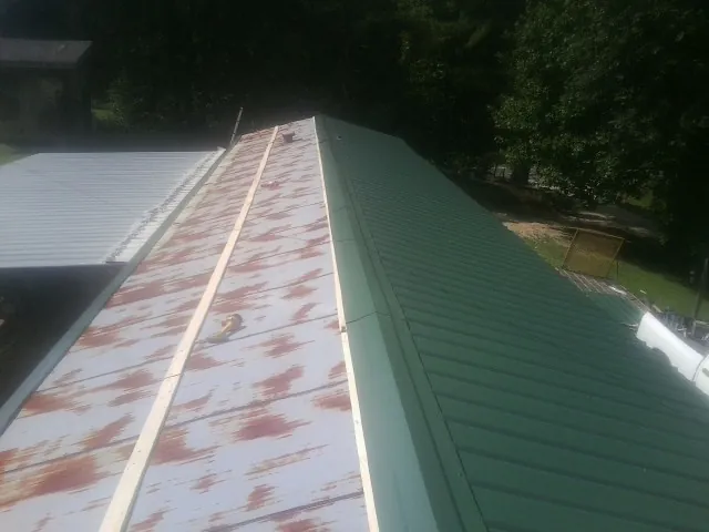 Old rusted panels beside newly installed green metal roofing — Wind Damage Roof Repair by Roofing Brothers in Parsonsfield