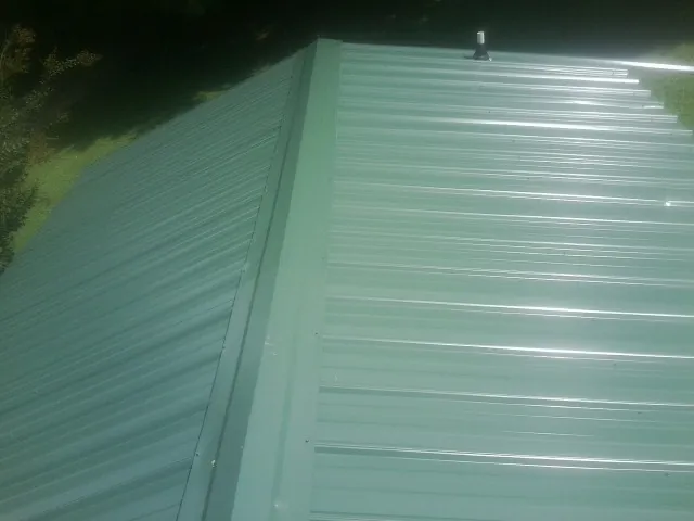 New green metal panels meeting at the ridge of a roof — Flat Roof Repair work by our crew in Parsonsfield