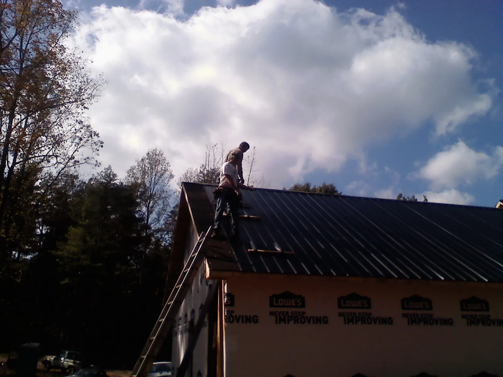 Roofer fastening dark metal panels high against a cloudy sky, from a Roof Inspection job in Parsonsfield
