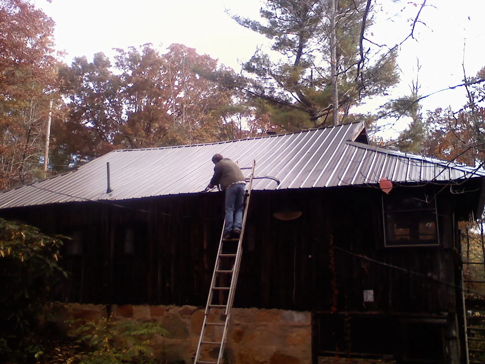 Roofer on a ladder working along the edge of a cabin metal roof in Parsonsfield