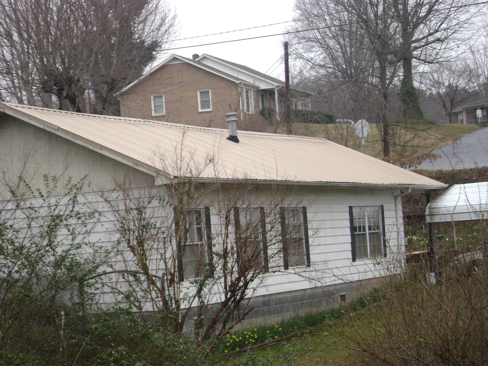 Tan metal roof on a white sided house set into a hillside — Commercial Roofing by Roofing Brothers in Parsonsfield